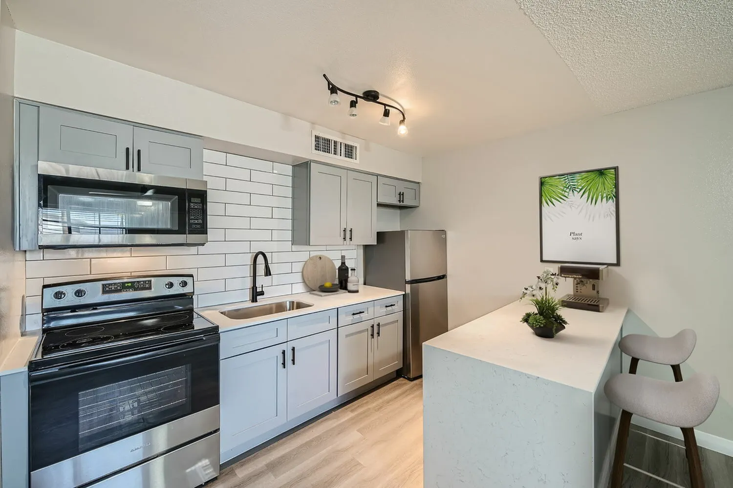 Kitchen, light blue shaker cabinetry, quartz countertops, stainless appliances, subway tile backsplash, wood-style plank flooring