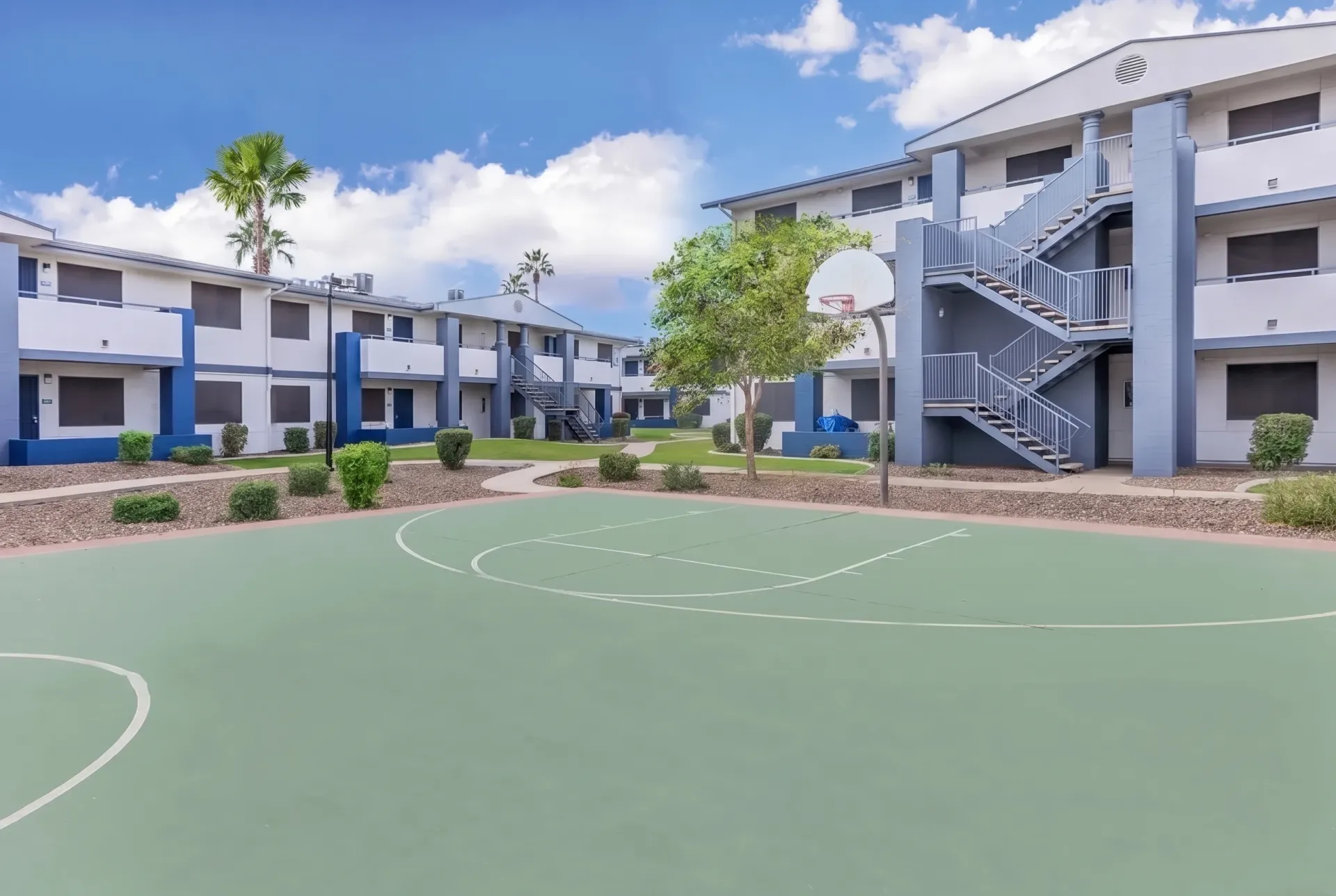 Basketball court, white painted lines, green surface, surrounding apartment buildings, palm tree, landscaping