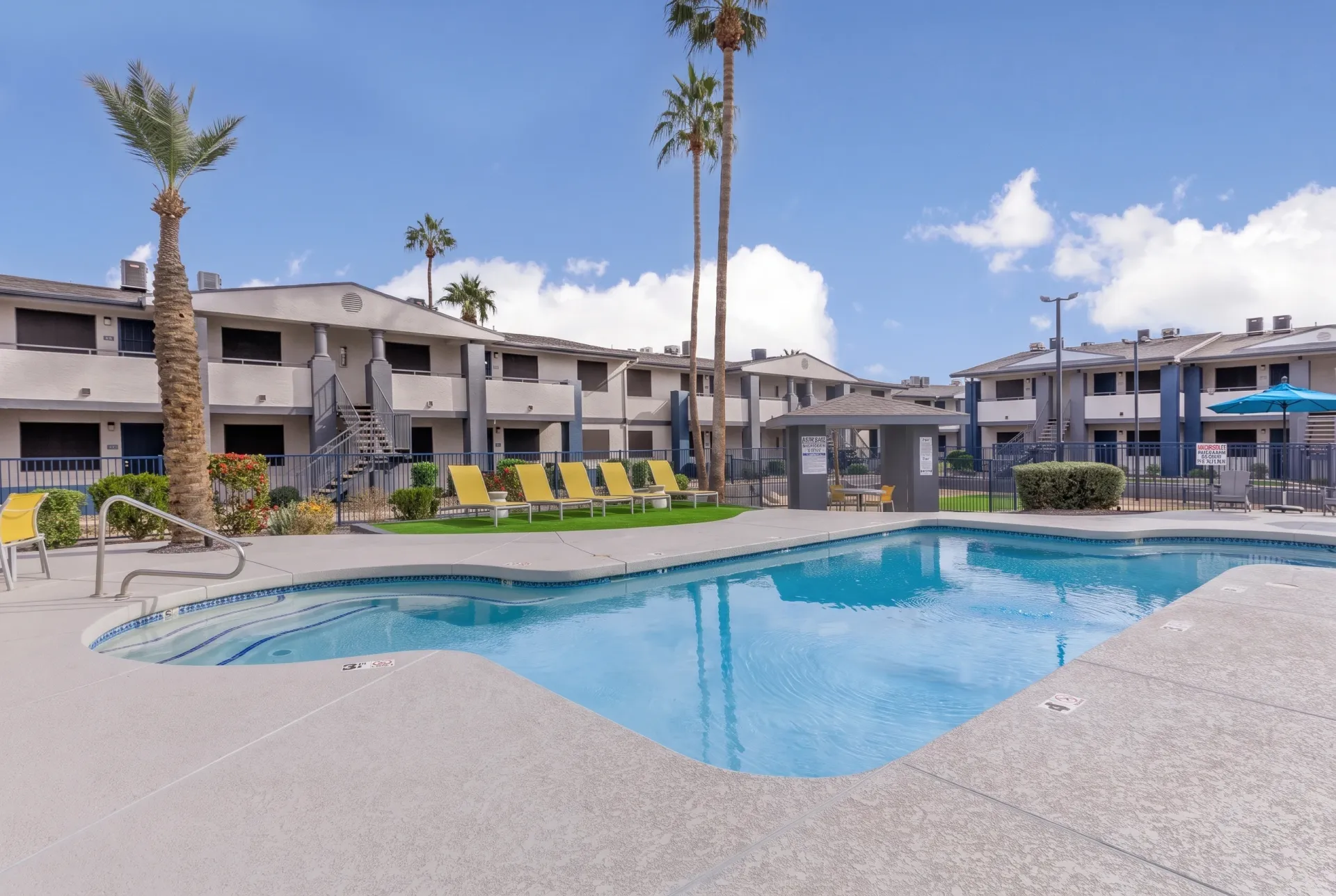 Swimming pool with lounge chairs, palm trees, apartment buildings, clear sky