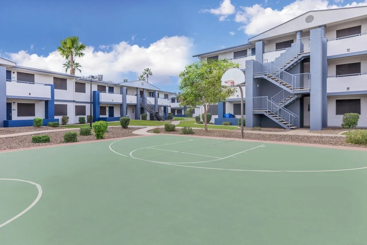 Basketball court, white painted lines, green surface, surrounding apartment buildings, palm tree, landscaping