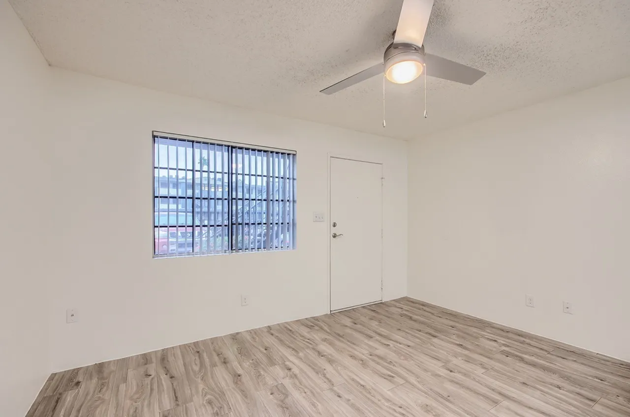 Bedroom, wood-style plank flooring, ceiling fan, barred window, entry door
