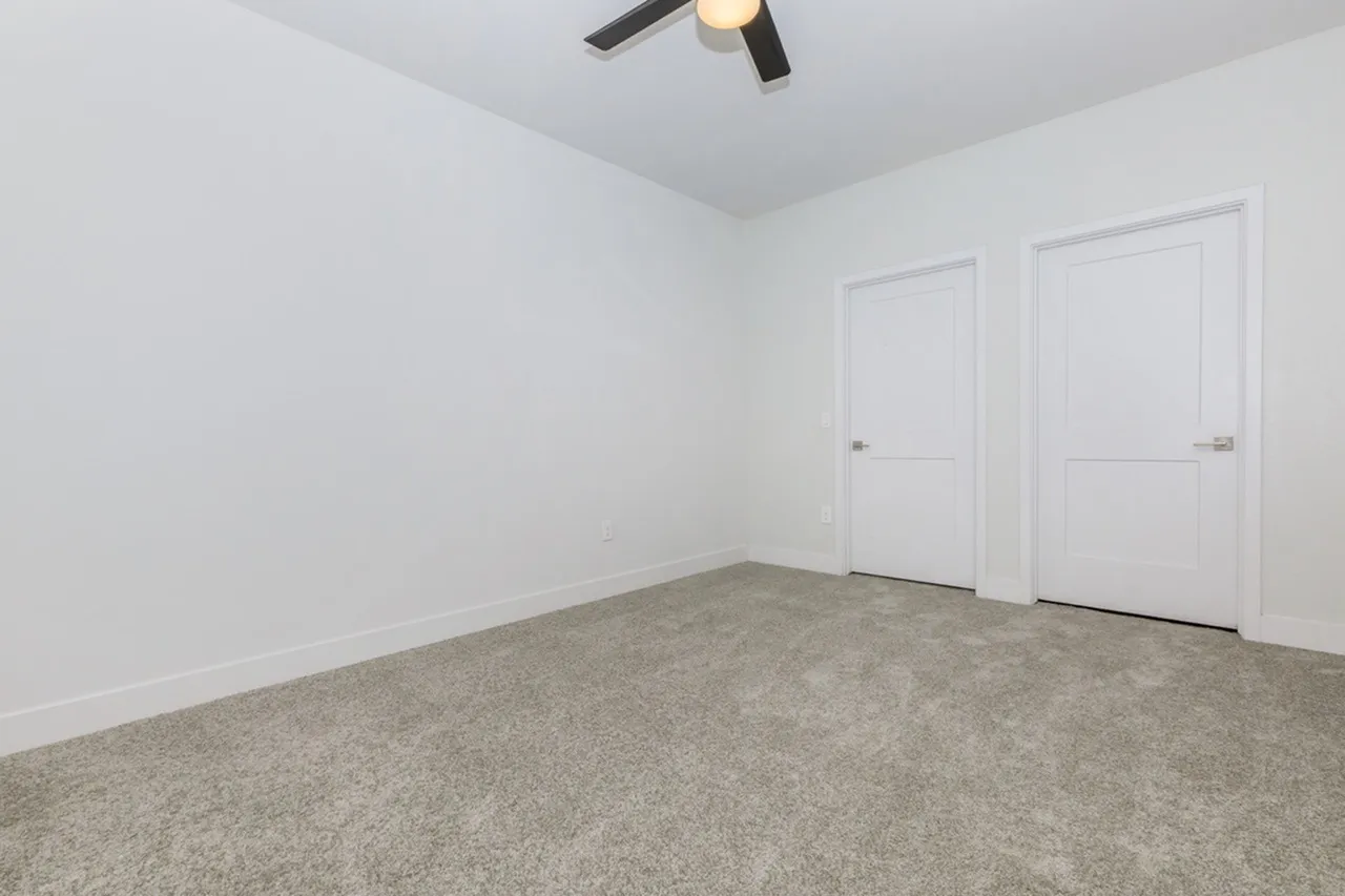 Bedroom, gray carpet flooring, two white closet doors, ceiling fan