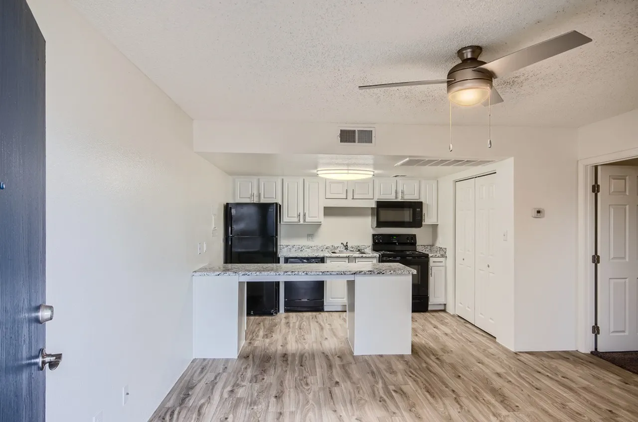 Kitchen with white cabinetry, black stainless appliances, quartz countertops, wood-style plank flooring, ceiling fan