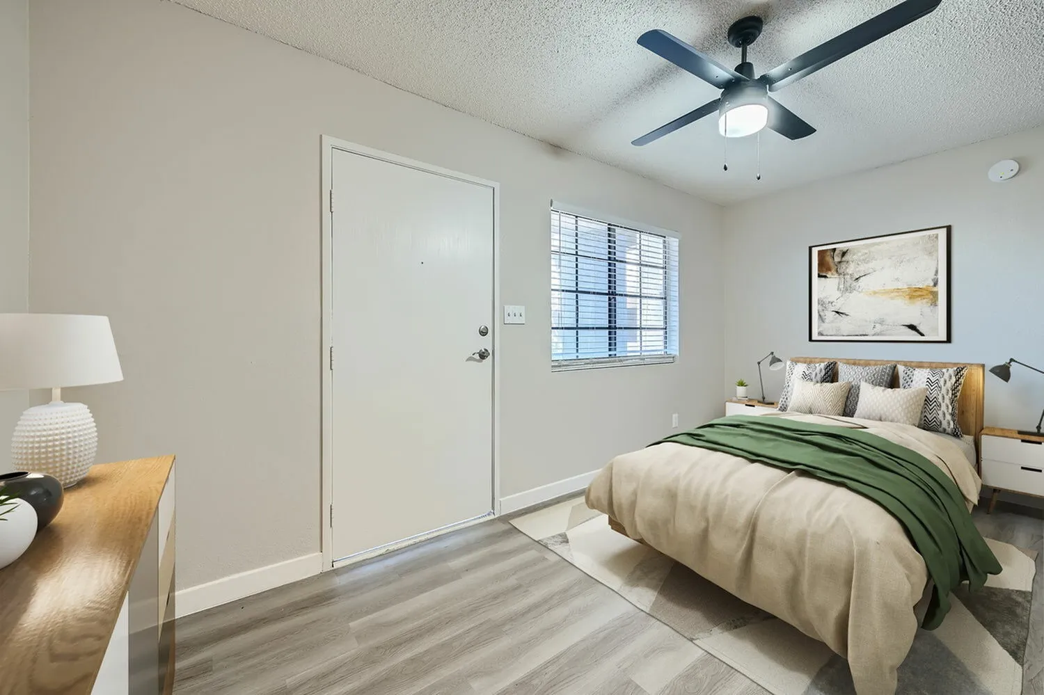 Primary bedroom, wood-style plank flooring, ceiling fan, entry door, green bedding