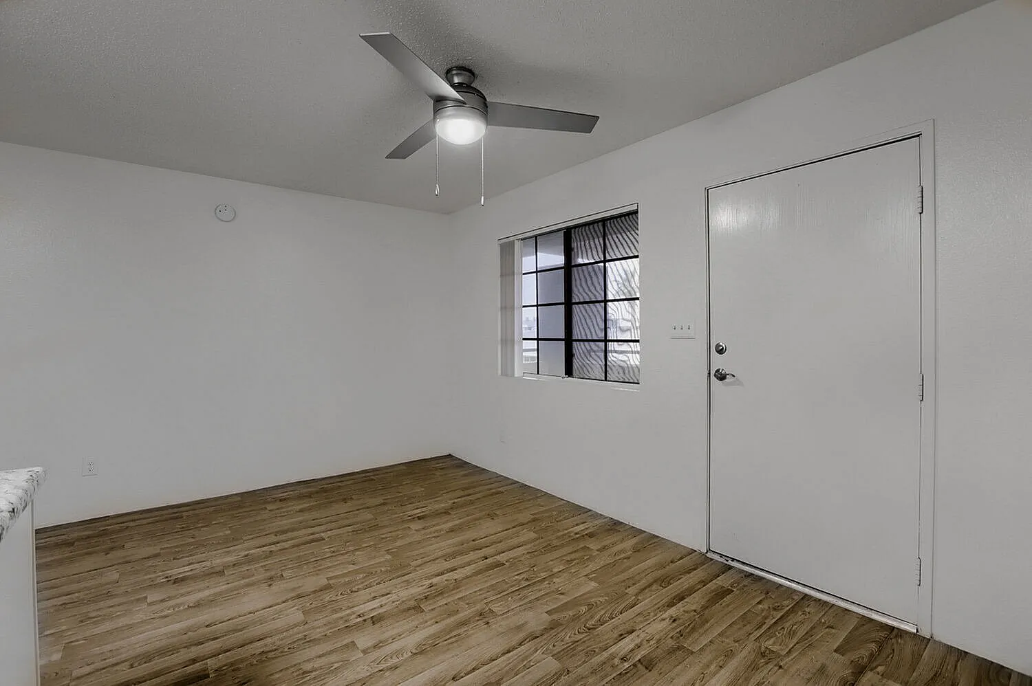 Bedroom, wood-style plank flooring, ceiling fan with light, white door, window with blinds