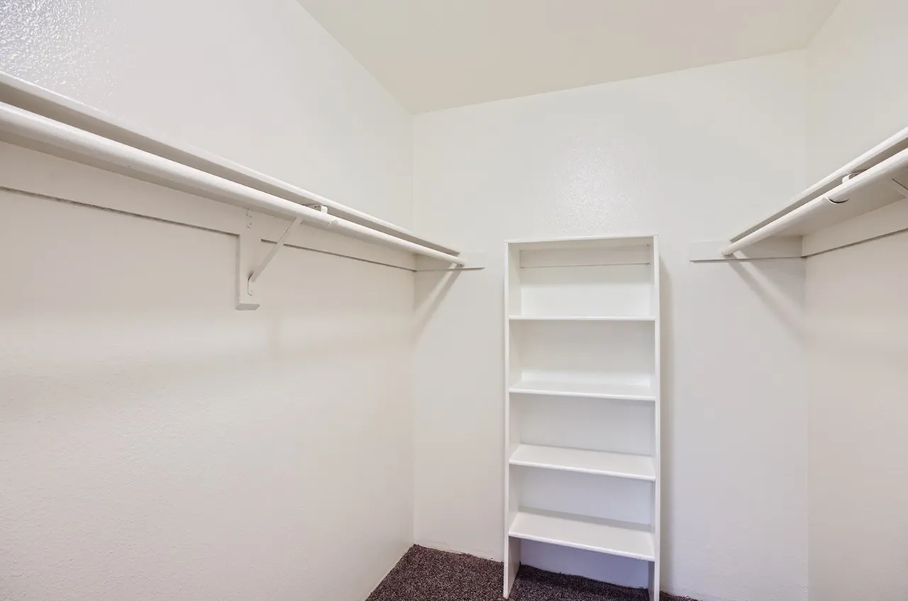 Walk-in closet, white shelving unit, chrome rods, brown carpet flooring