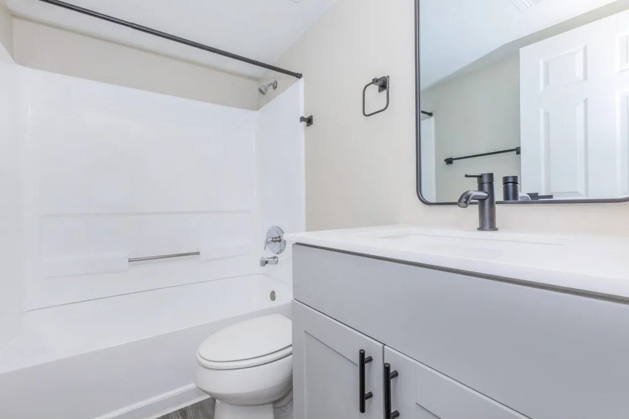 Bathroom, gray vanity with white countertop, black fixtures, mirrored medicine cabinet, shower-tub combination