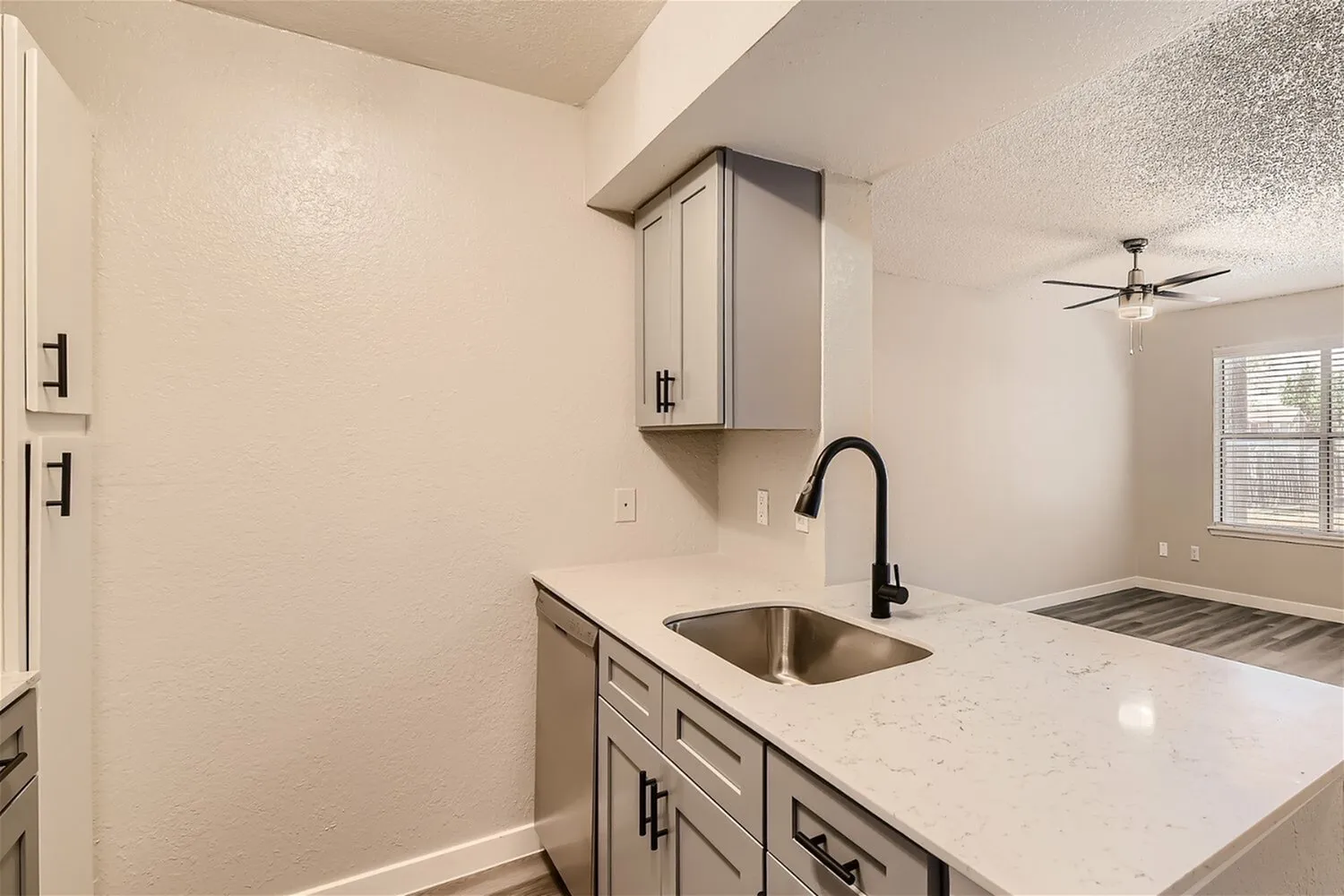 Undermount sink, black gooseneck faucet, white countertop, gray cabinetry