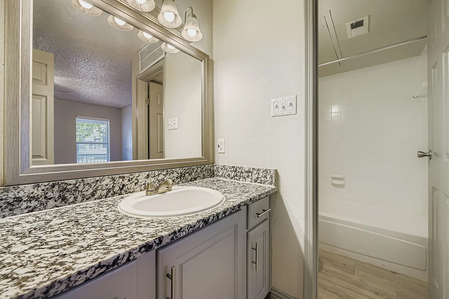 Bathroom vanity, framed mirror, drop-in sink, speckled countertop, gray cabinet