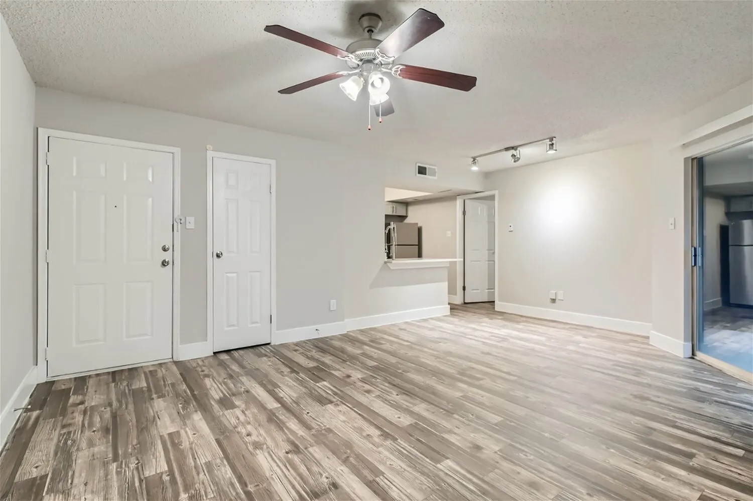 Living area, ceiling fan, entry door, closet door, breakfast bar, wood-style plank flooring