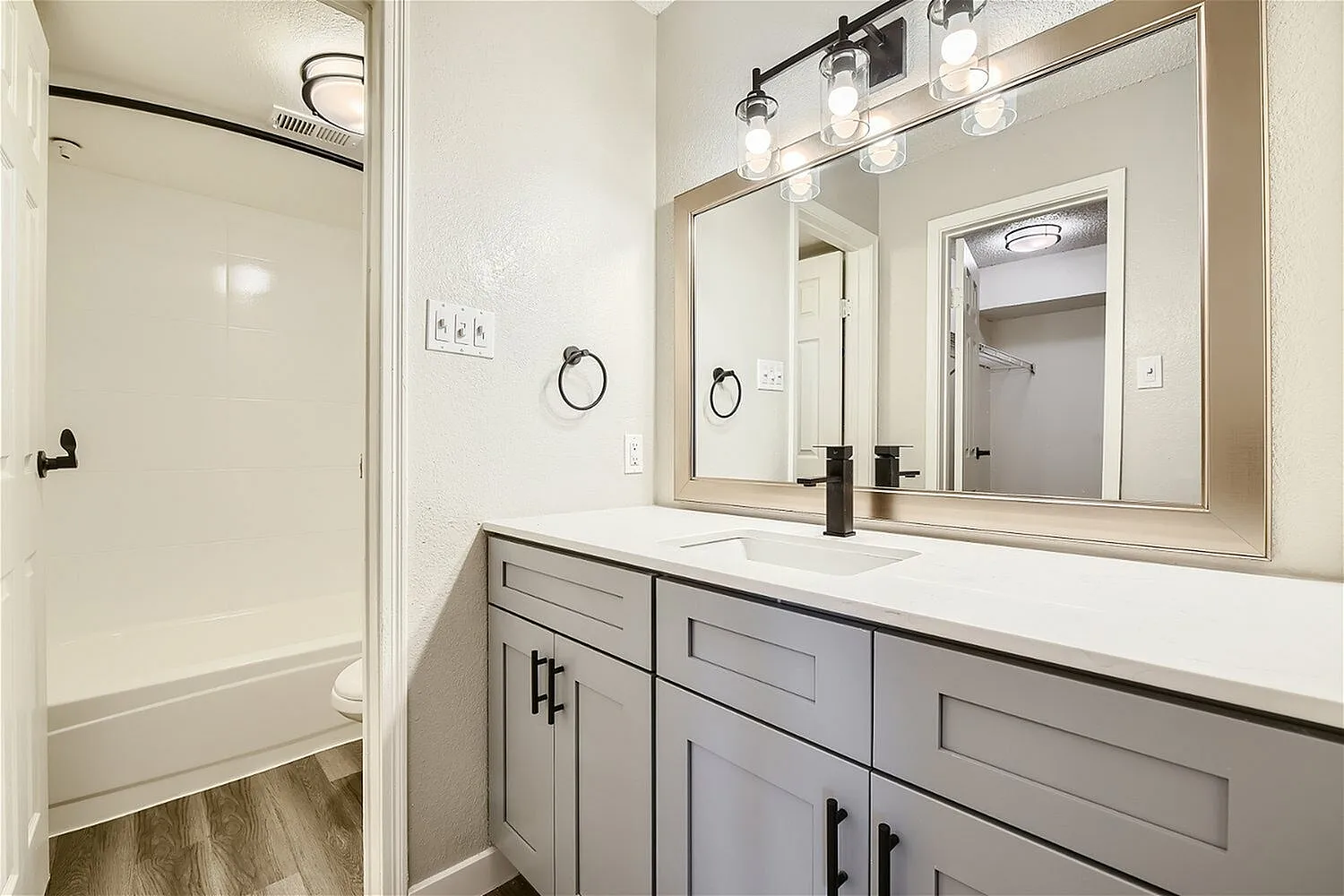 Bathroom vanity, vanity light fixture, framed mirror, gray cabinet, tub shower