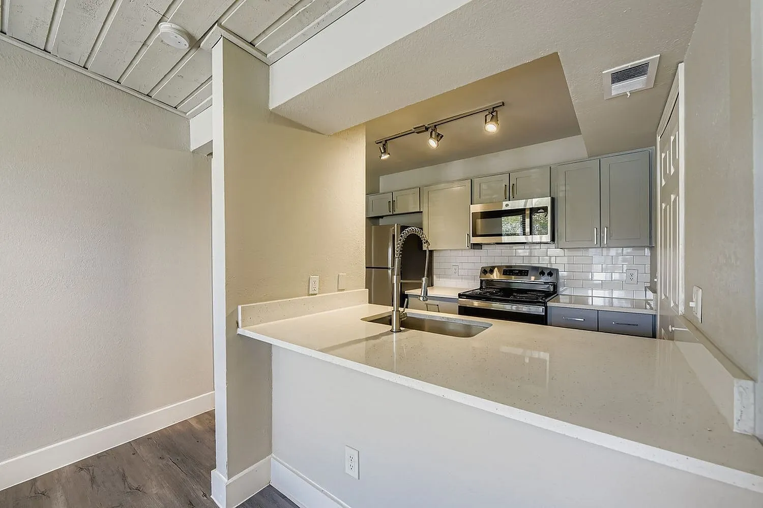 Kitchen, gray cabinetry, quartz-style peninsula, stainless steel appliances, subway tile backsplash, track lighting
