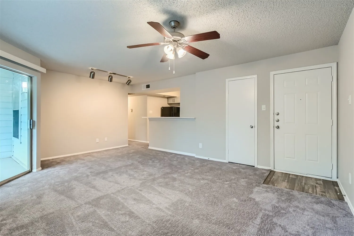 Open living area, ceiling fan, track lighting, breakfast bar, entry door, carpet flooring