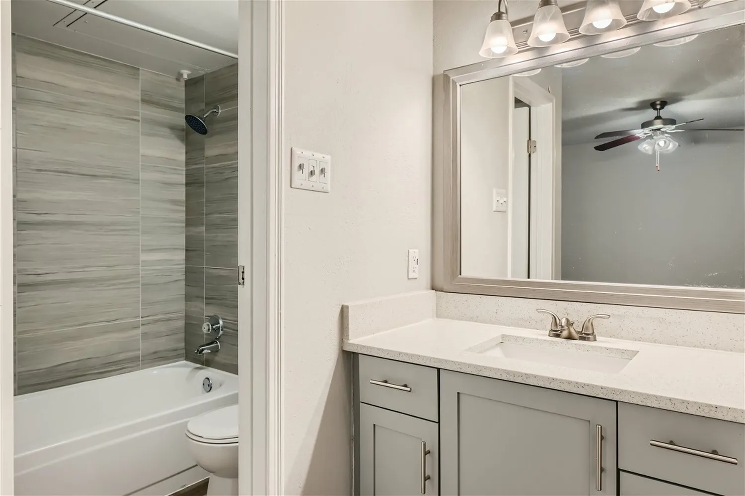 Bathroom vanity, framed mirror, quartz-style countertop, wood-look tile tub surround