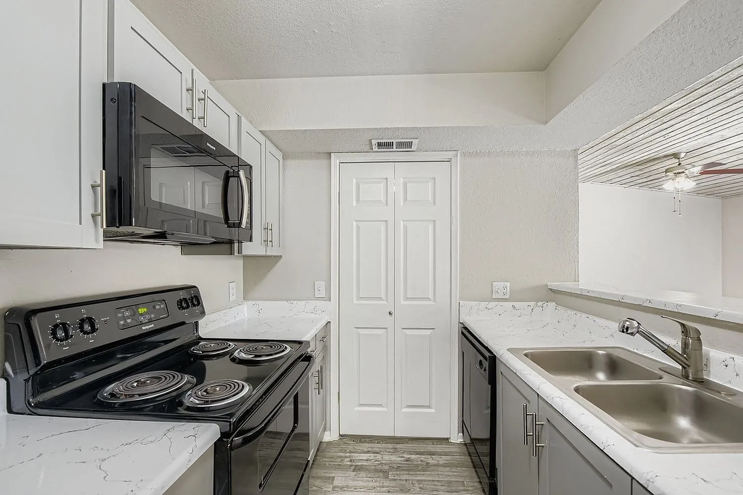Kitchen, black appliances, electric coil range, over-range microwave, white veined countertops, pantry doors