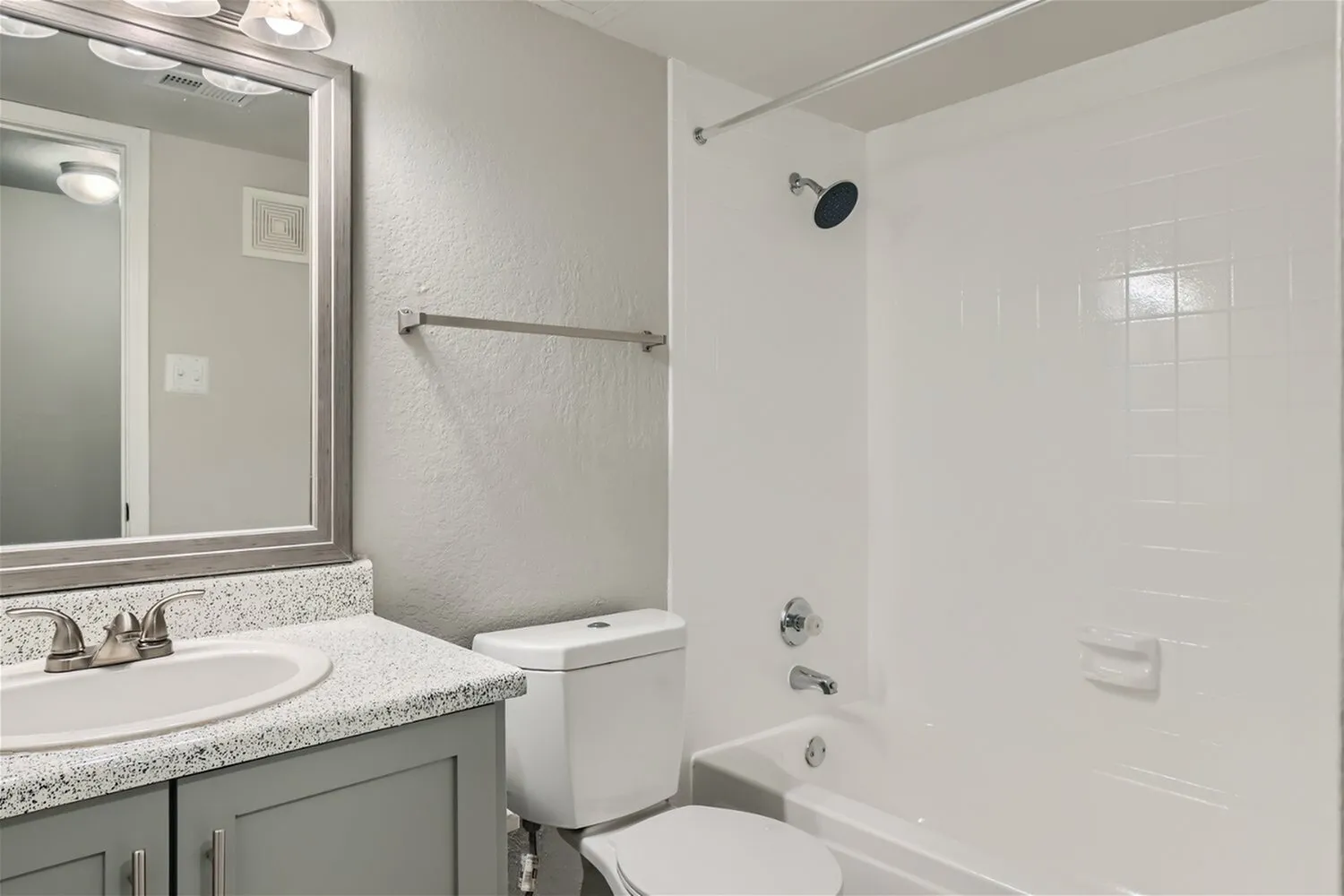 Tub shower, white surround, speckled vanity countertop, white toilet