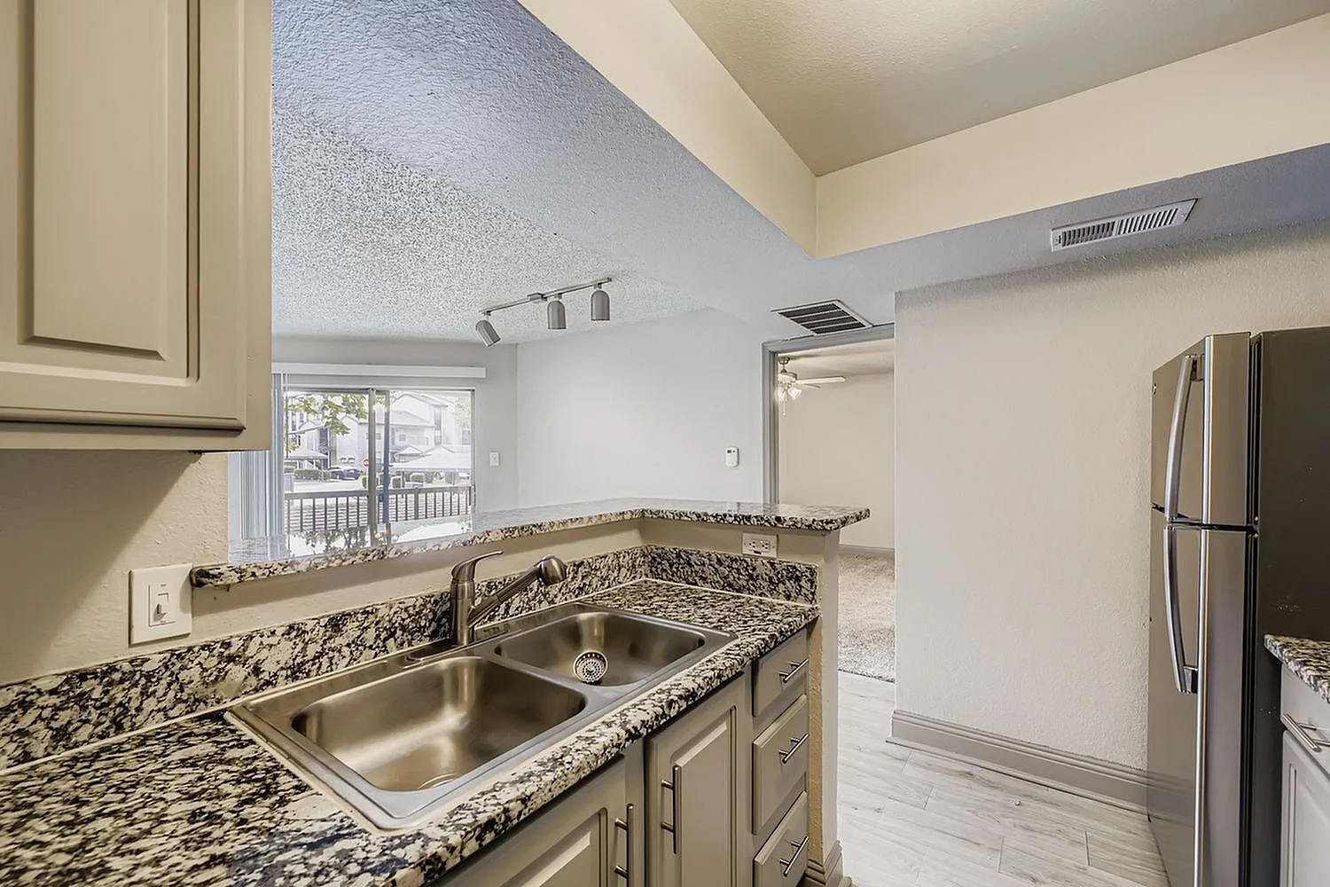 Double basin stainless steel sink, speckled countertop, track lighting, view to living room