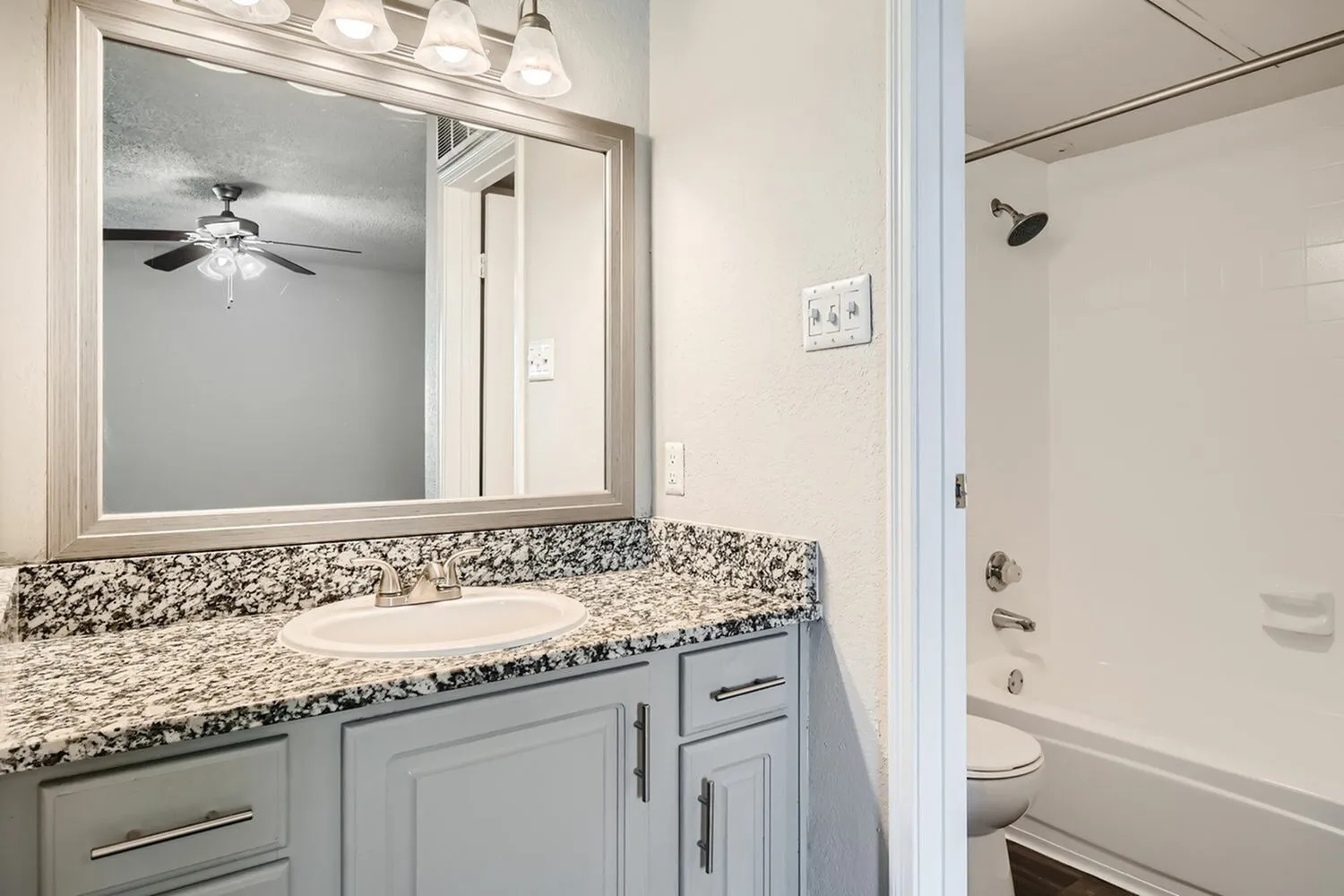 Bathroom vanity, framed mirror, speckled countertop, tub shower