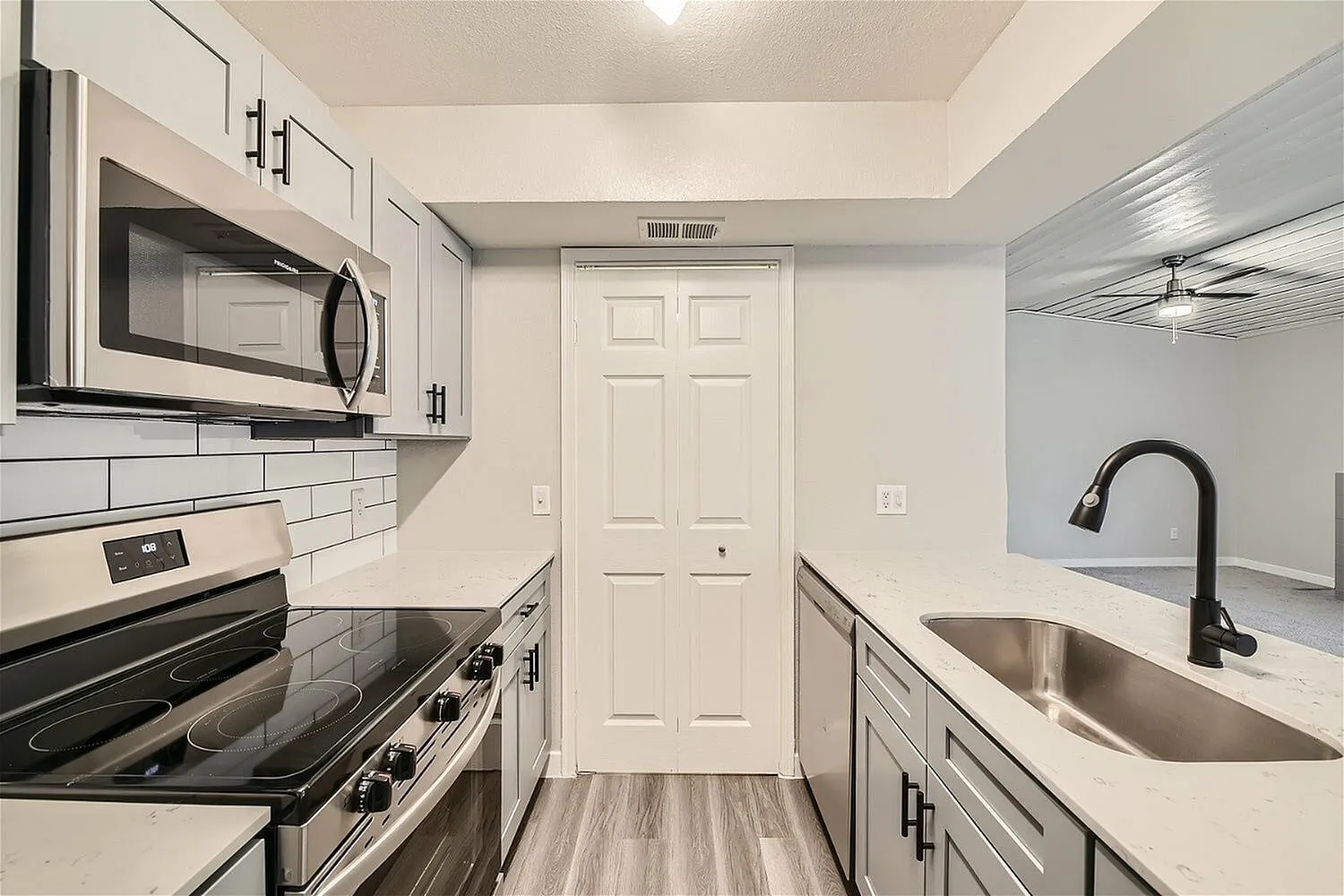 Galley kitchen, gray cabinetry, stainless steel microwave, glass-top range, subway tile backsplash, pantry door