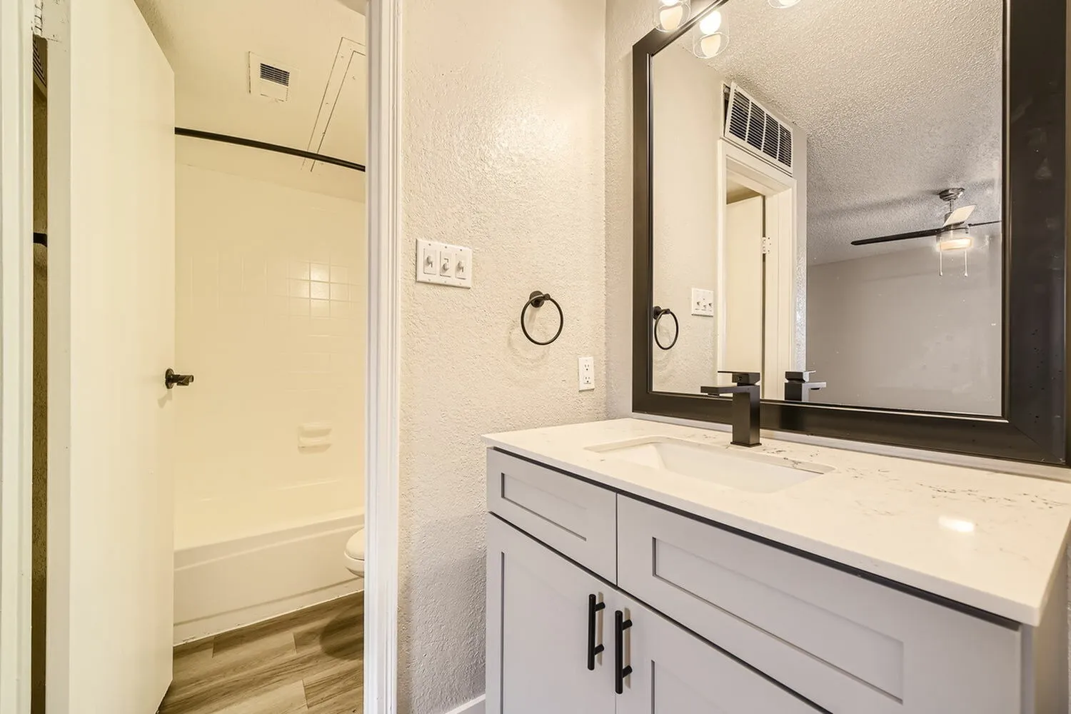 Bathroom vanity, black framed mirror, black faucet, quartz-style countertop, tub shower