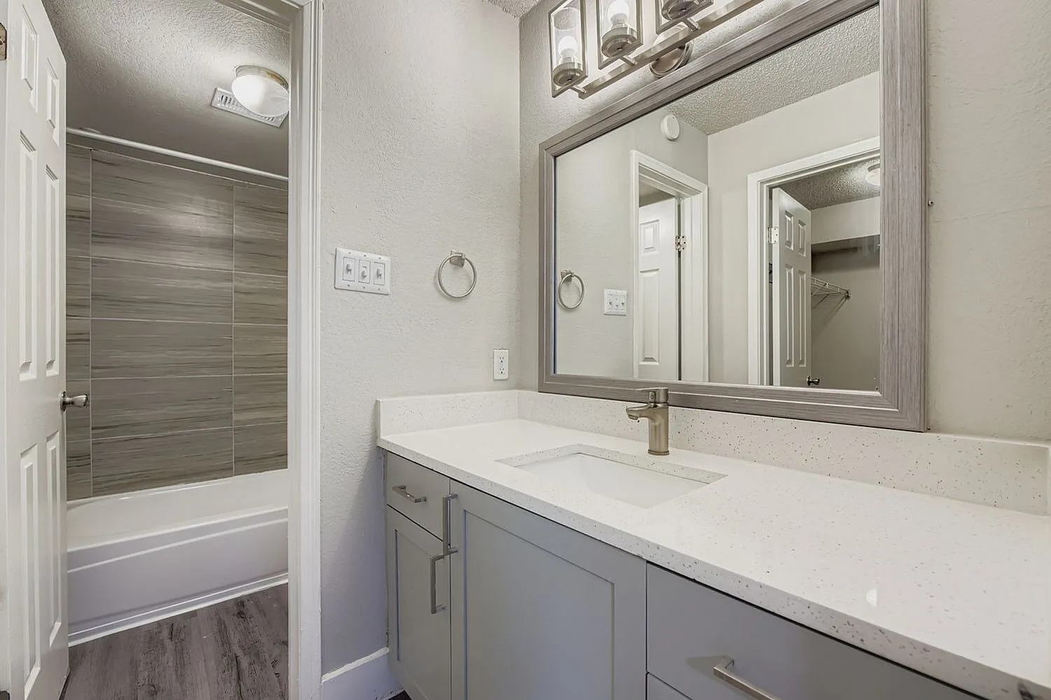 Bathroom vanity, framed mirror, quartz-style countertop, wood-look tile tub surround