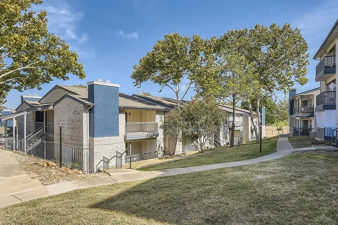 Brick and stucco apartment building, blue accent tower, walkway, mature trees