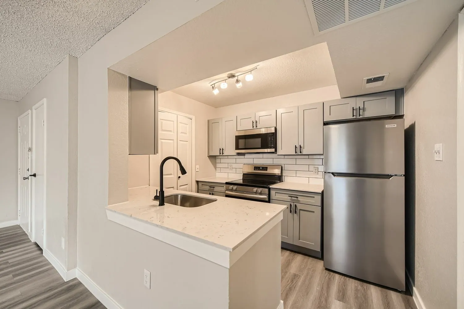 Kitchen, gray cabinetry, quartz-style peninsula countertop, stainless steel appliances, subway tile backsplash, track lighting