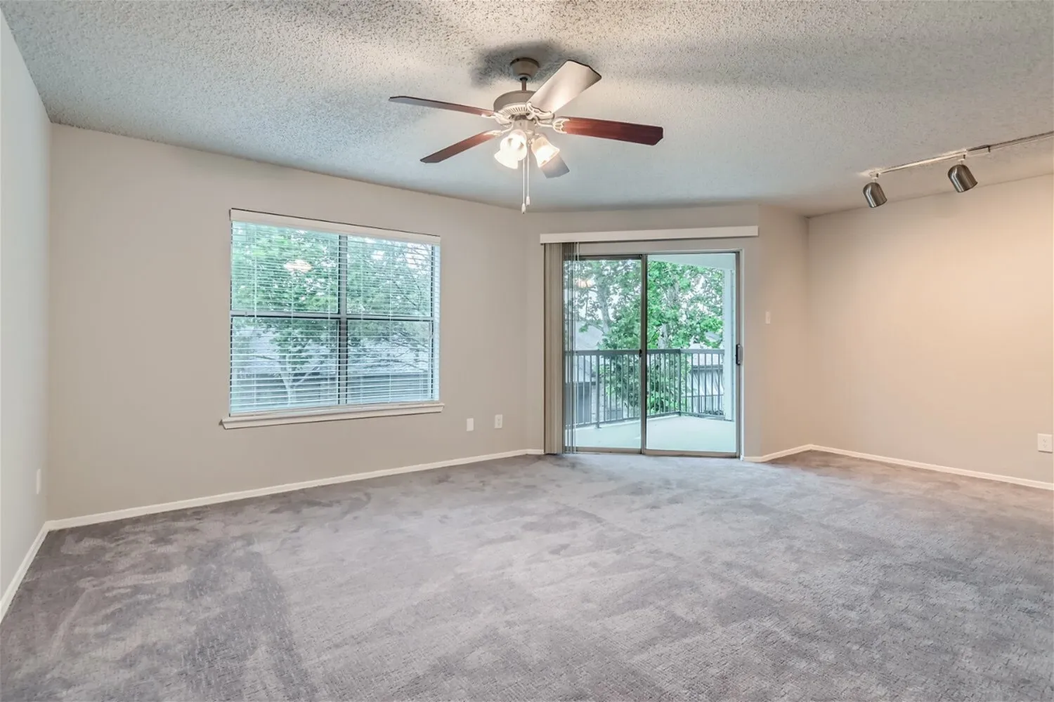 B1 Classic living room, ceiling fan, window with blinds, sliding glass door to balcony, carpet flooring