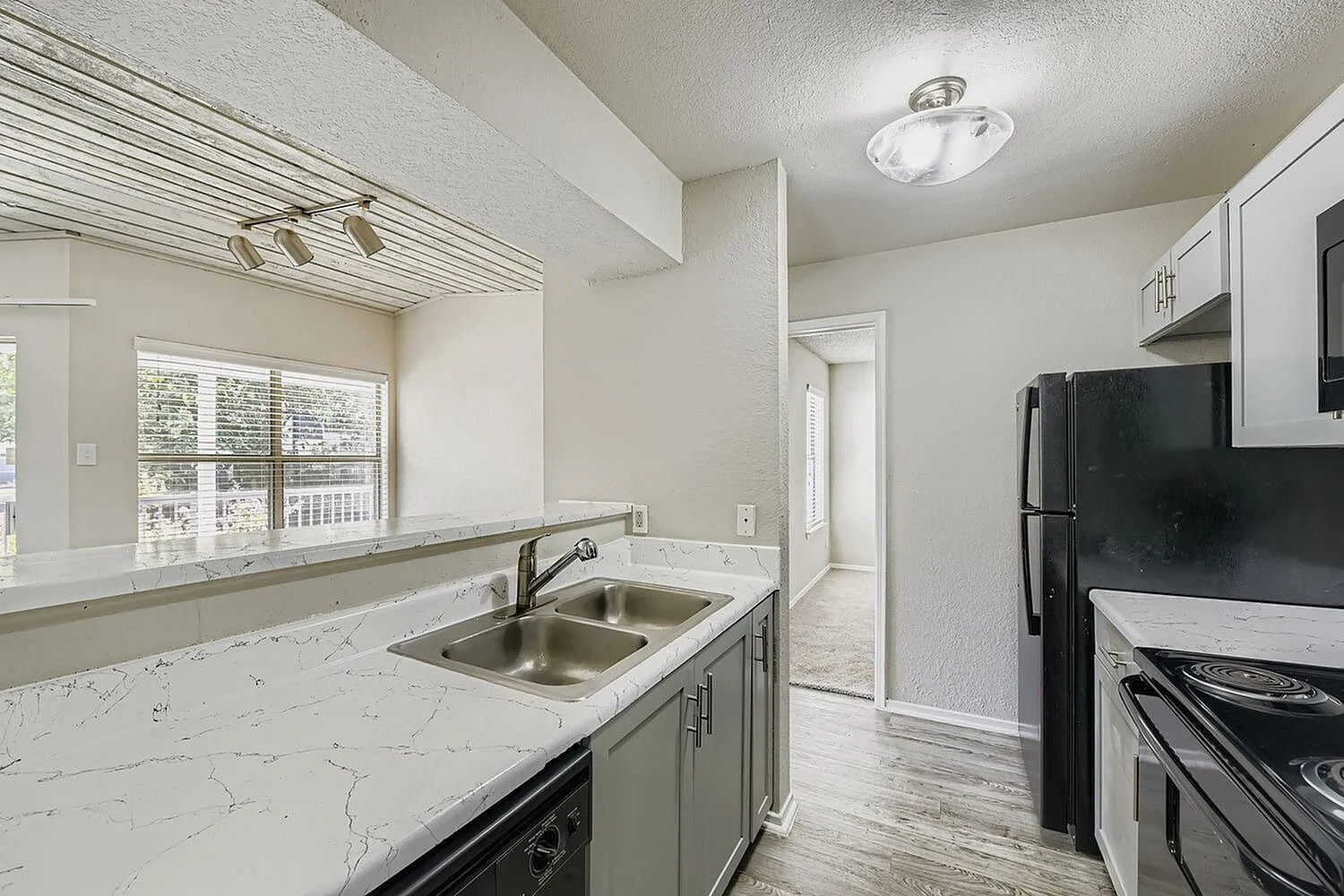 Double basin sink, white veined countertop, breakfast bar, window, track lighting