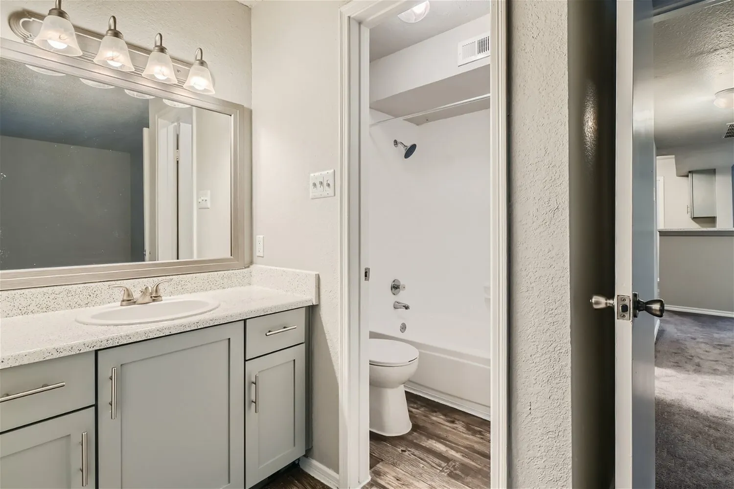 Bathroom vanity, framed mirror, gray cabinet, speckled countertop, tub shower