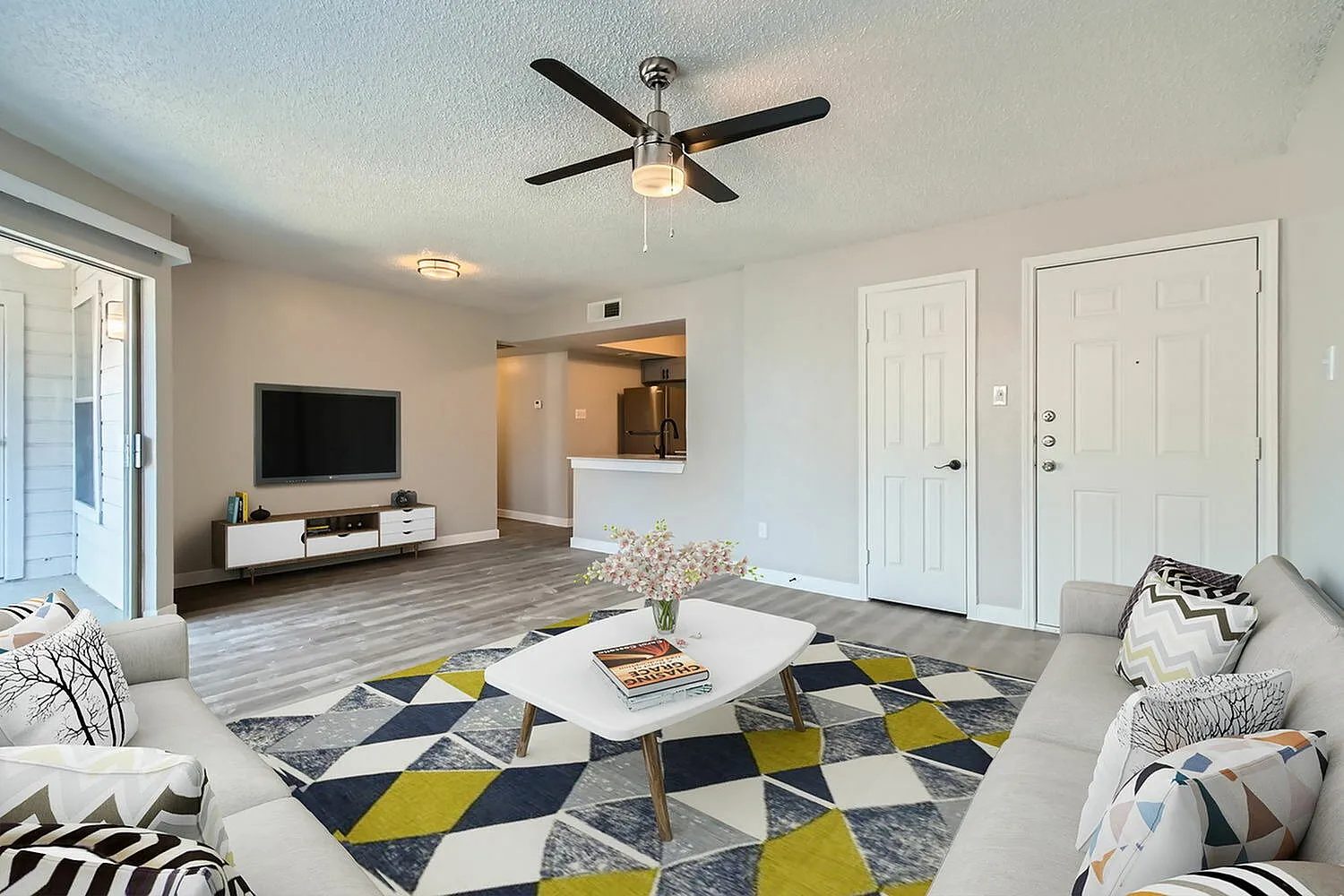 Living room, ceiling fan, entry door, coat closet door, kitchen beyond, wood-style plank flooring