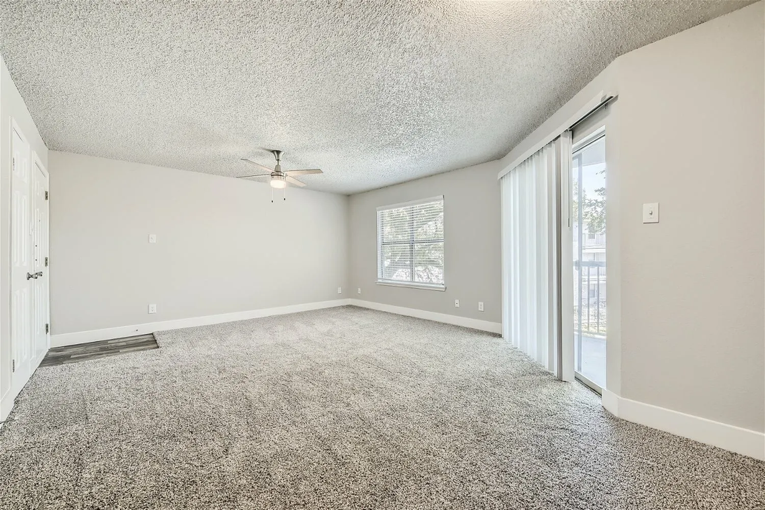Living room, ceiling fan, window, sliding glass door with vertical blinds, carpet flooring