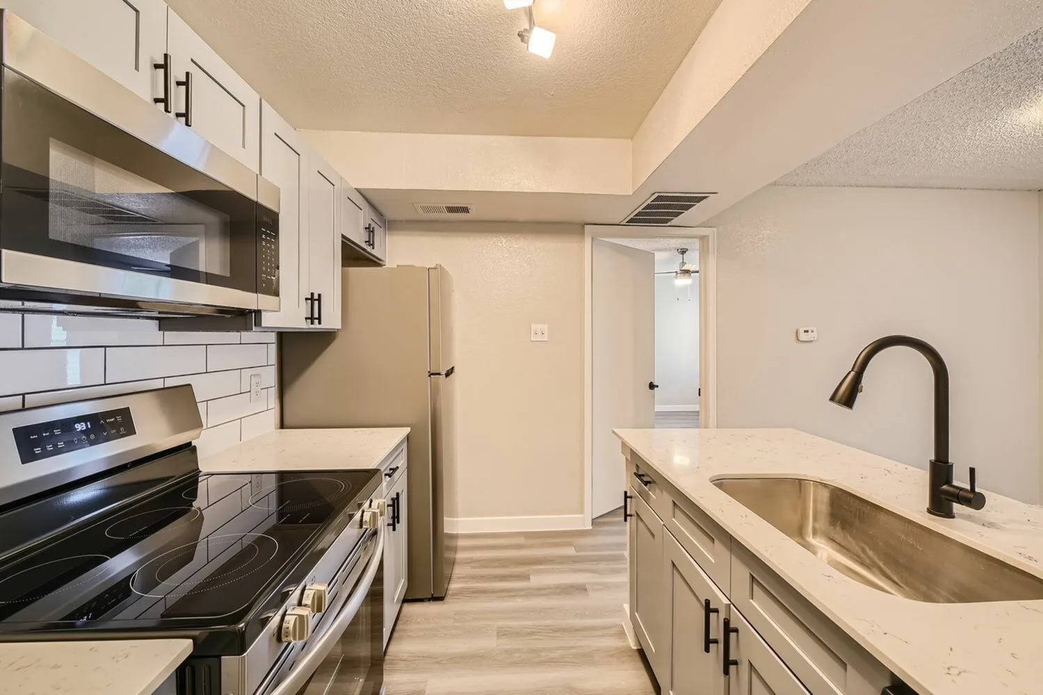 Kitchen, stainless steel refrigerator, over-range microwave, tile backsplash, view to hallway, wood-style plank flooring