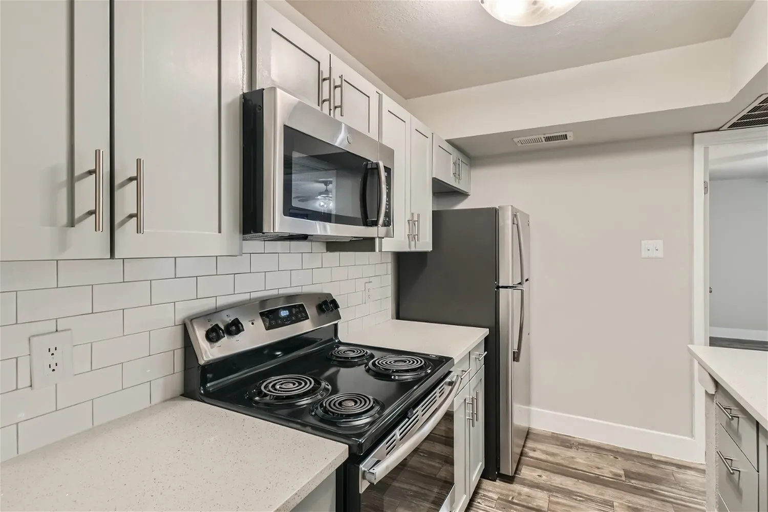 Stainless steel microwave, electric coil range, subway tile backsplash, refrigerator