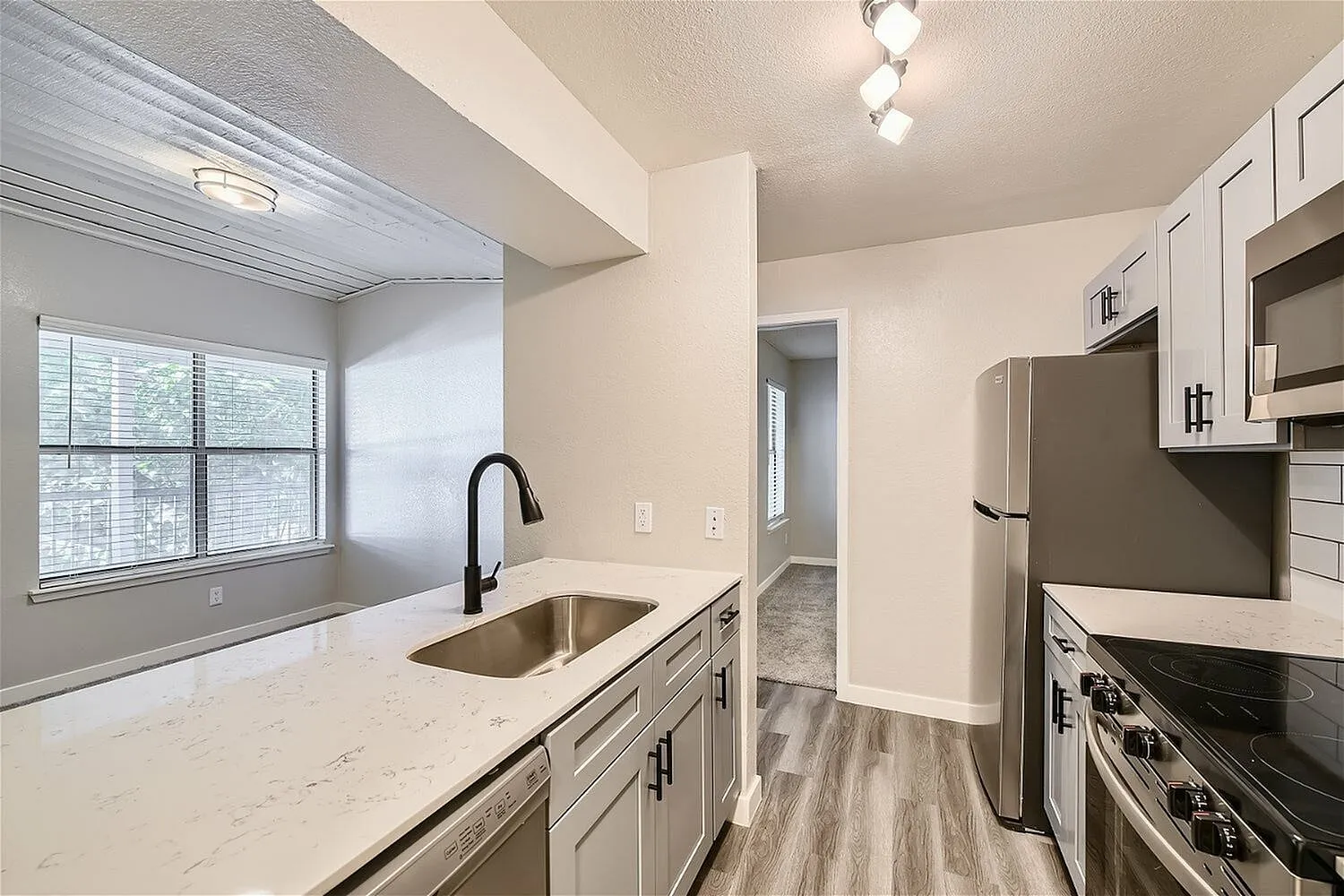 Undermount sink, black gooseneck faucet, quartz-style countertop, window, wood-style plank flooring