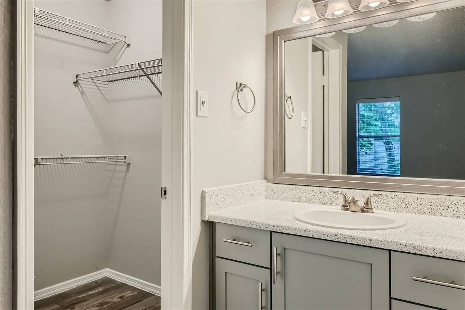 Bathroom vanity, drop-in sink, speckled countertop, framed mirror, wire shelving closet