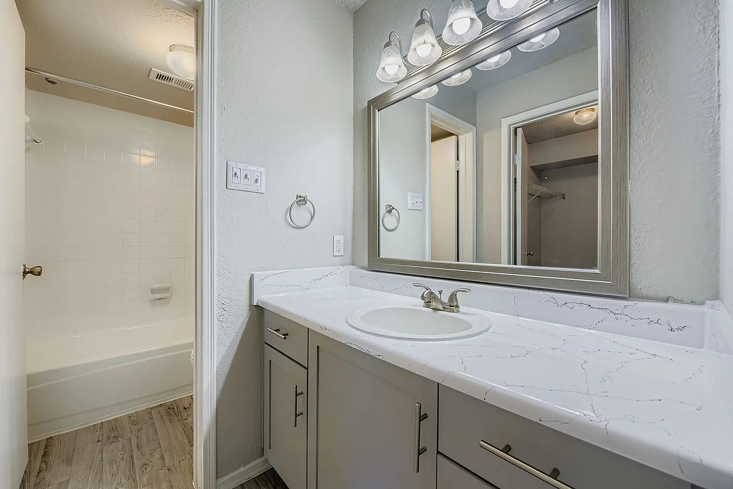 Bathroom vanity, framed mirror, drop-in sink, white veined countertop, closet view
