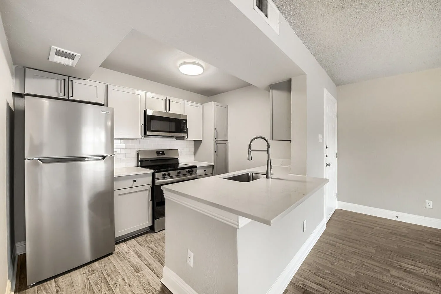 Kitchen, gray cabinetry, white quartz-style peninsula, stainless steel appliances, pull-down faucet