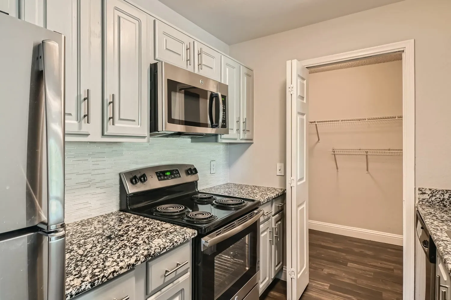 Kitchen, stainless steel microwave, electric coil range, speckled countertop, tile backsplash, walk-in closet door
