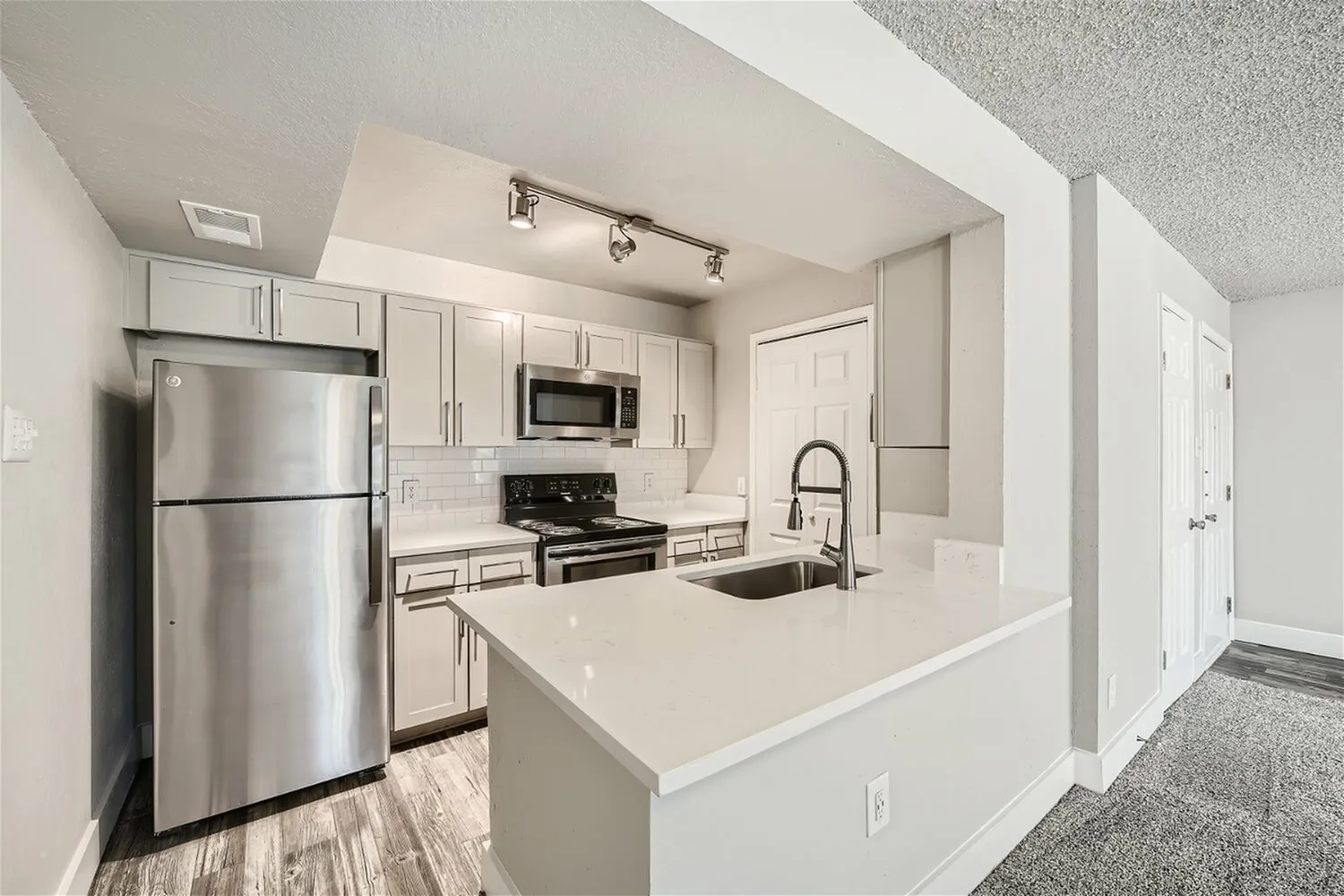 Kitchen, white cabinetry, quartz-style peninsula, stainless steel appliances, subway tile backsplash, track lighting
