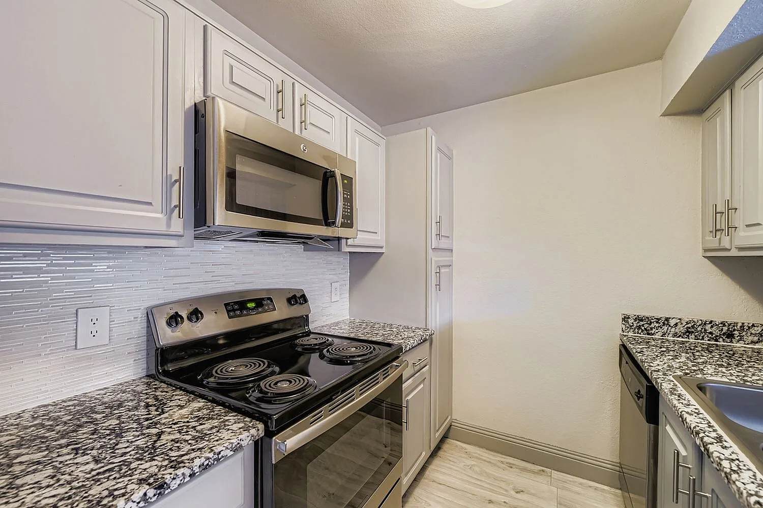 Stainless steel microwave, electric coil range, tile backsplash, speckled countertop