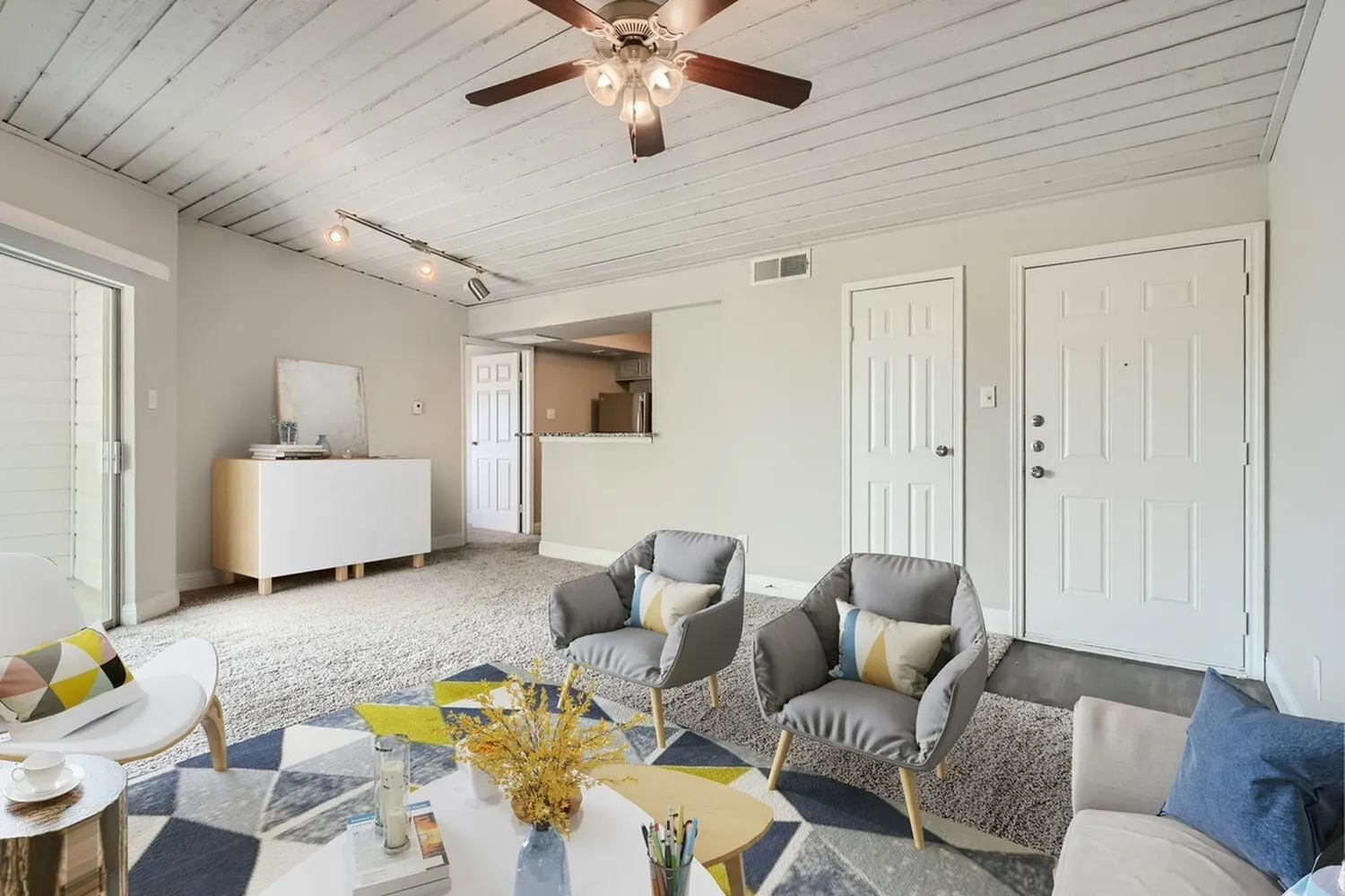 Living area, plank ceiling, track lighting, entry door, closet door, breakfast bar, carpet flooring