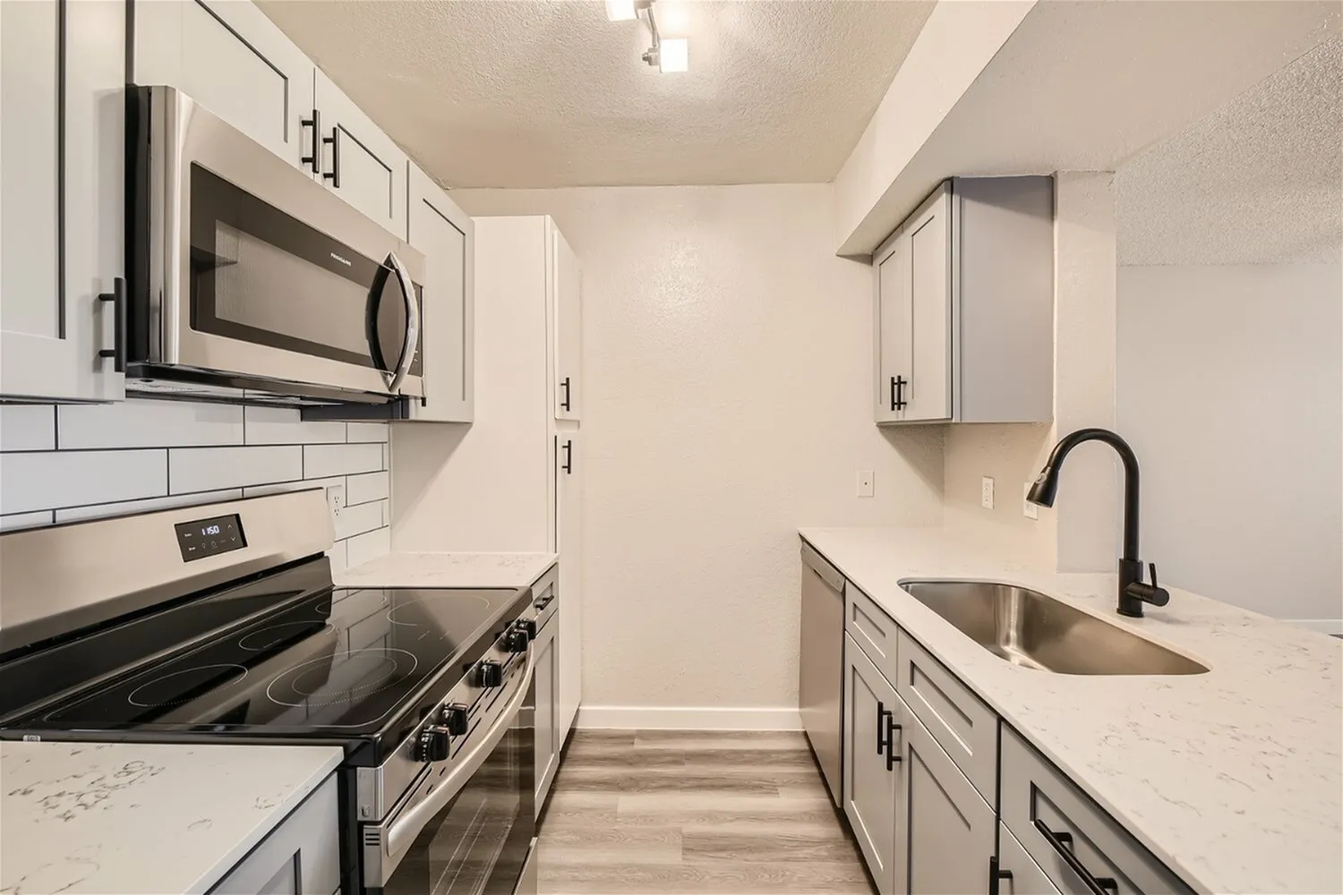 Glass-top range, over-range microwave, gray cabinets, wood-style plank flooring