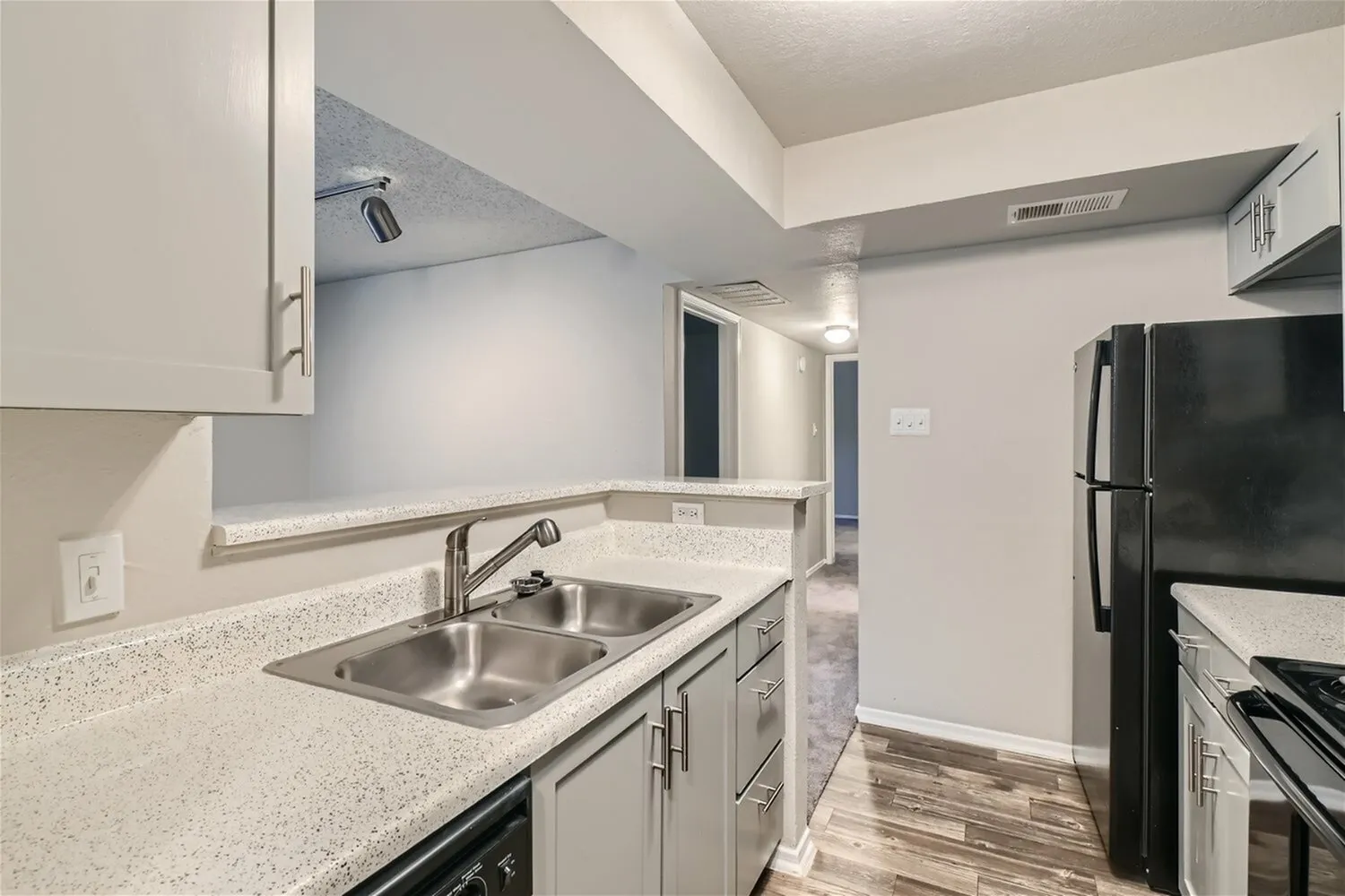 Double basin stainless steel sink, speckled countertop, gray cabinetry, hallway view