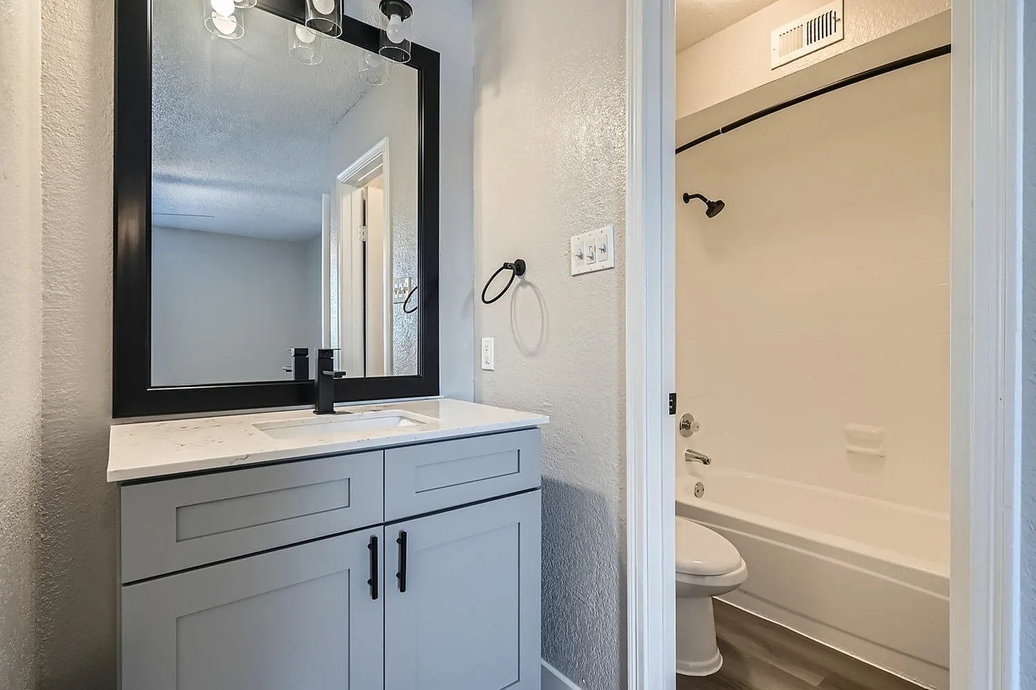 Bathroom vanity, black framed mirror, black faucet, quartz-style countertop, tub shower with black fixtures