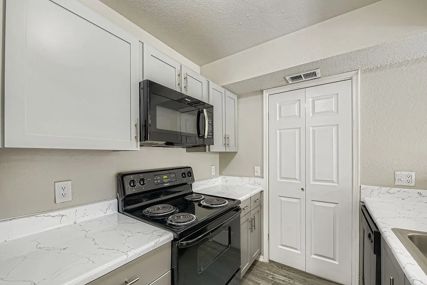 Black microwave, electric coil range, gray cabinetry, white veined countertop, pantry doors