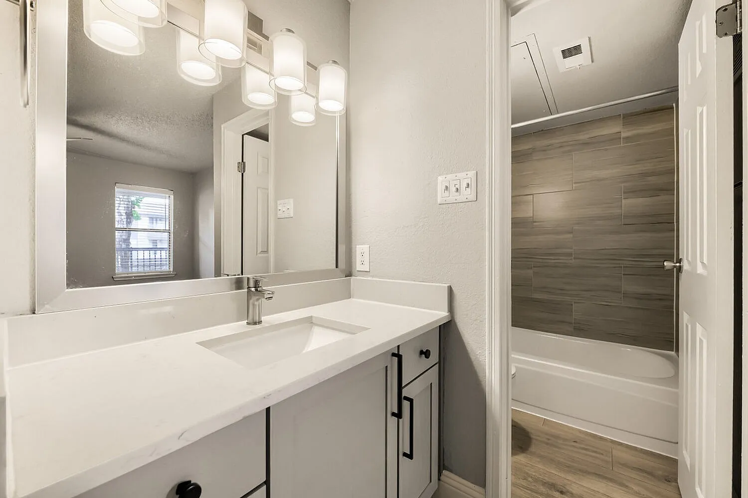 Bathroom vanity, framed mirror, undermount sink, quartz-style countertop, wood-look tile tub surround