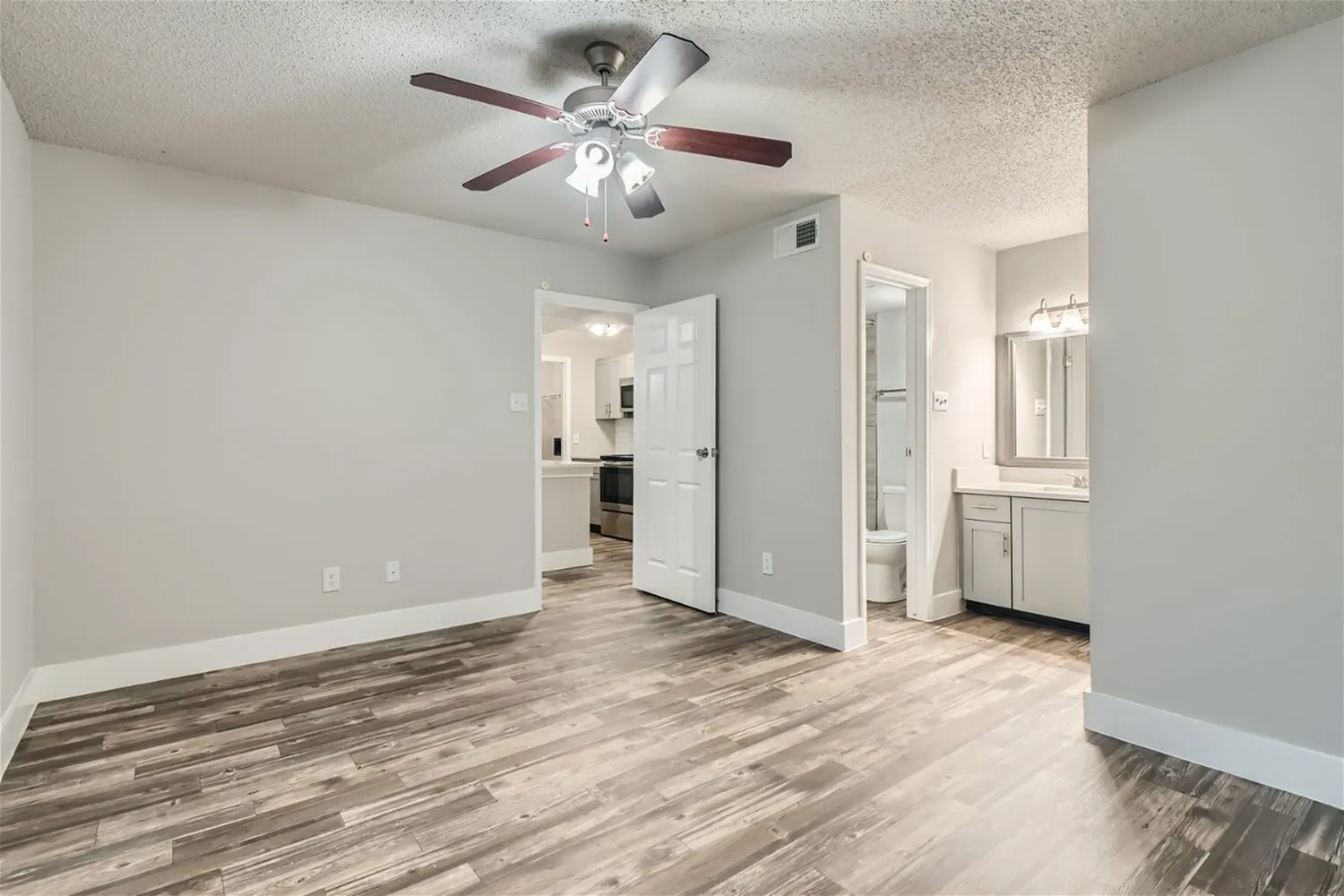 Bedroom, ceiling fan, doorway to bathroom, wood-style plank flooring