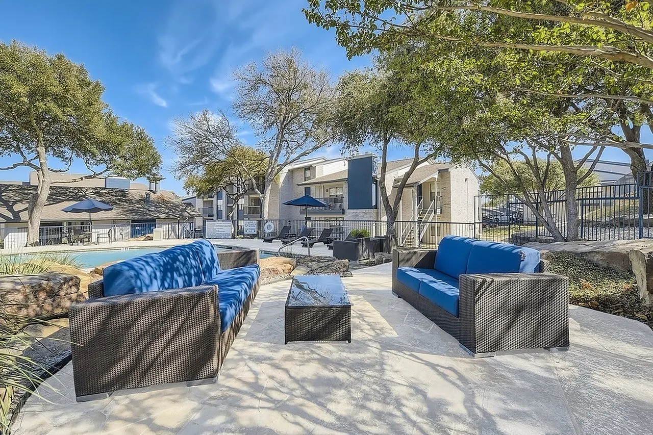 Outdoor lounge area, sofa seating, coffee table, mature trees, apartment buildings