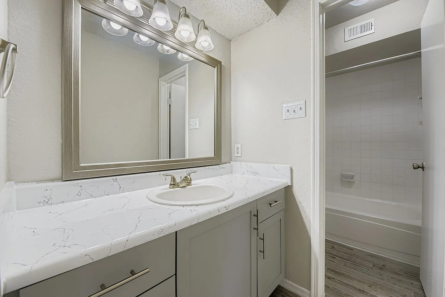 Bathroom vanity, framed mirror, white veined countertop, tub shower